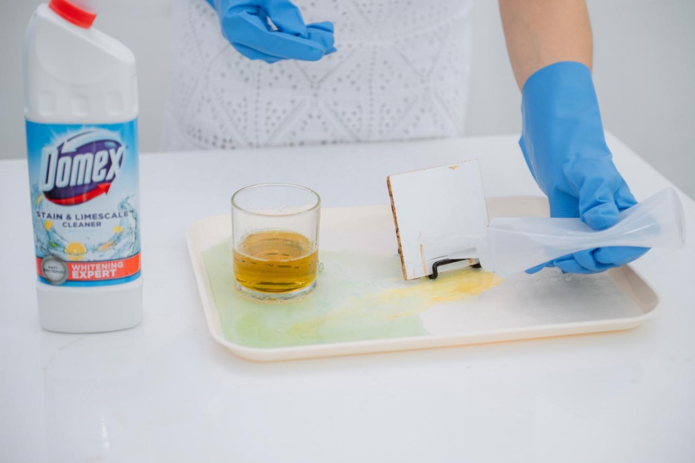 A person wearing blue gloves cleaning a tray with a glass of liquid Description automatically generated